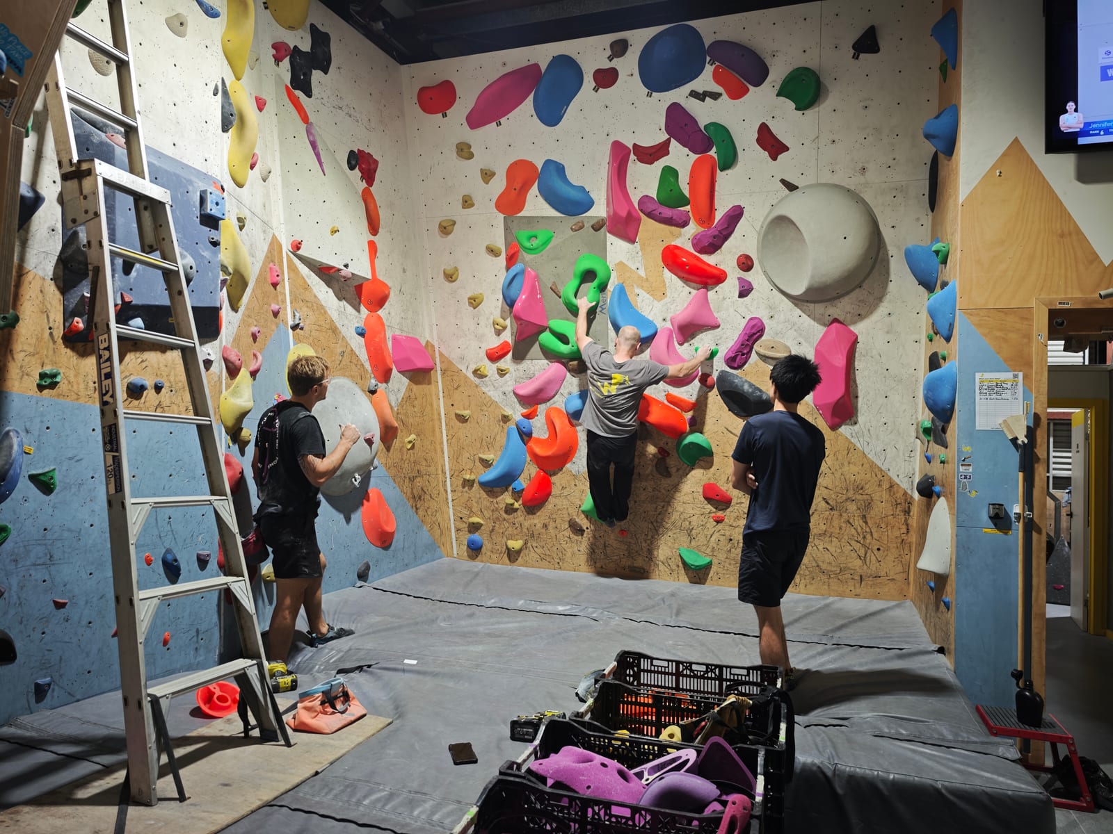 Three route setters working together on a bouldering wall inside Wall Walkers.